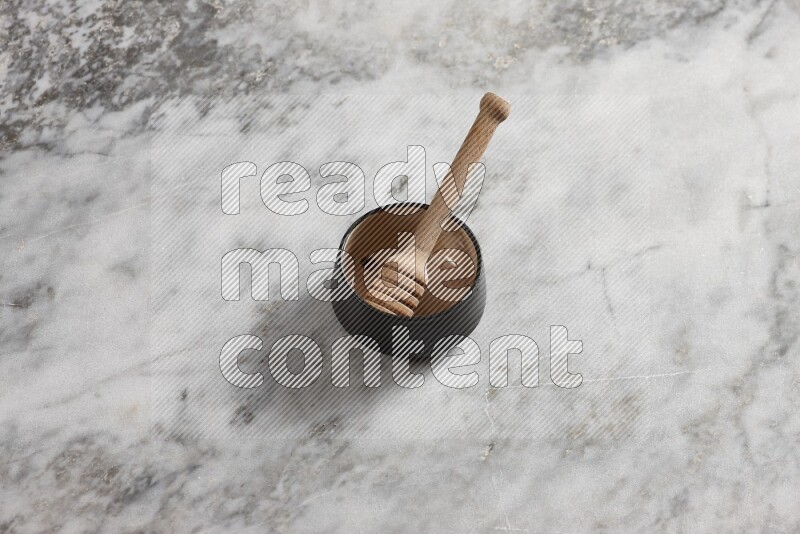 Black pottery bowl with wooden honey dipper in it on grey marble background