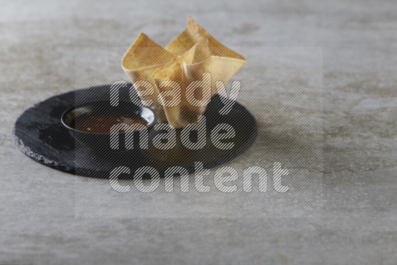 wonton cups with soy sauce ramkin on circle slate on grey textured counter top
