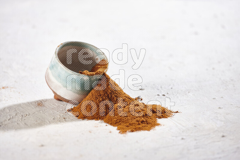 A colored pottery bowl full of ground paprika powder with fallen powder from it on white background