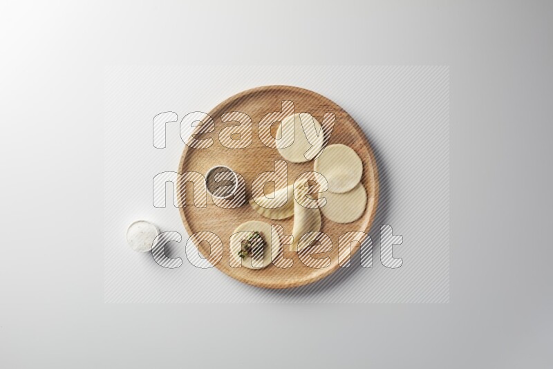 two closed sambosas and one open sambosa filled with meat while salt and black pepper aside in a wooden dish on a white background