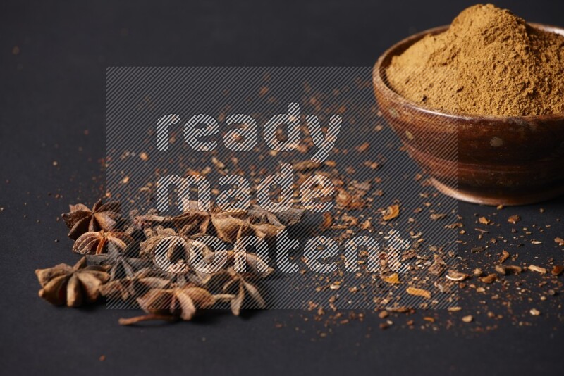 Star Anise powder in a wooden bowl with star anise beside it on a black background