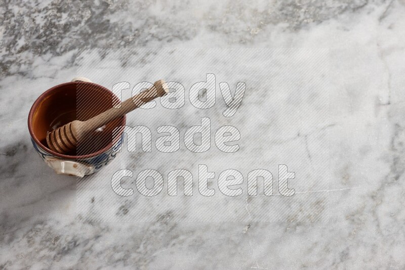 Decorative pottery pot with wooden honey dipper in it on grey marble background