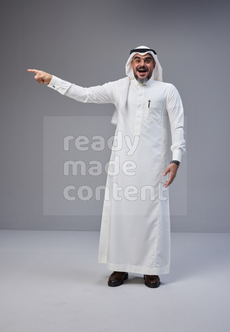 Saudi man Wearing Thob and white Shomag standing interacting with the camera on Gray background
