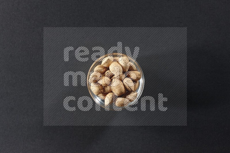 A glass bowl full of almonds on a black background in different angles