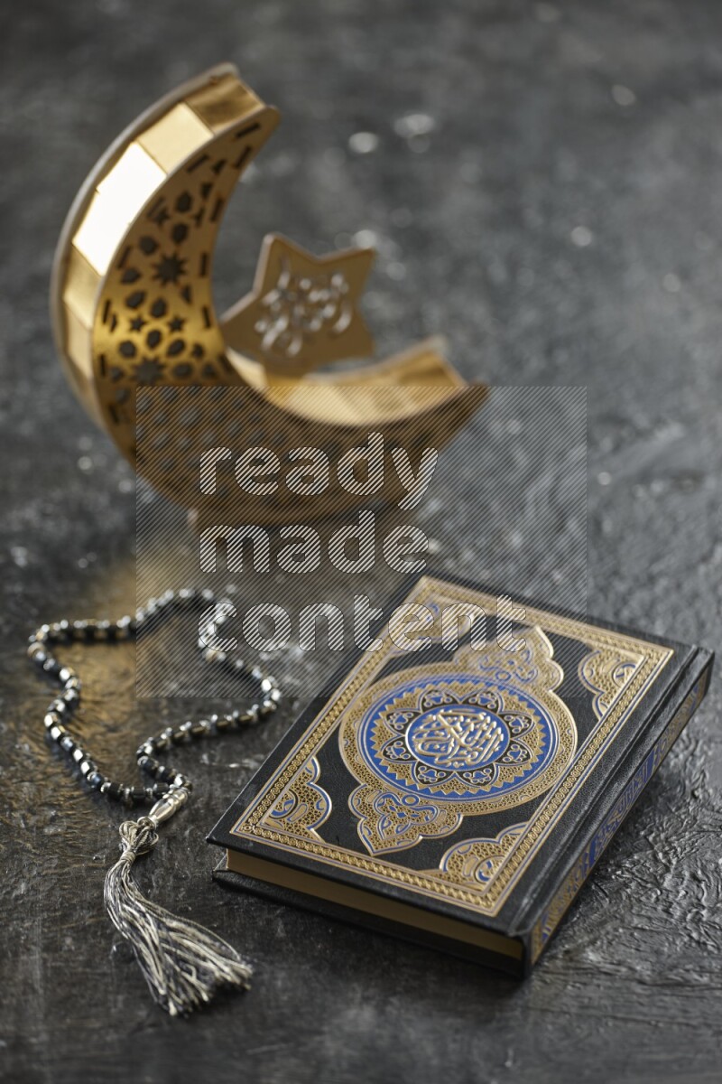 A wooden golden crescent lantern with different drinks, dates, nuts, prayer beads and quran on textured black background