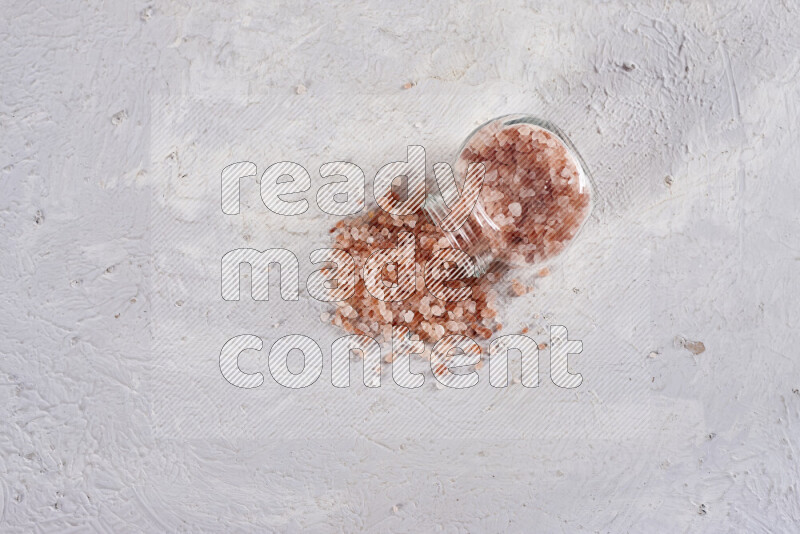 A glass jar full of coarse himalayan salt crystals on white background
