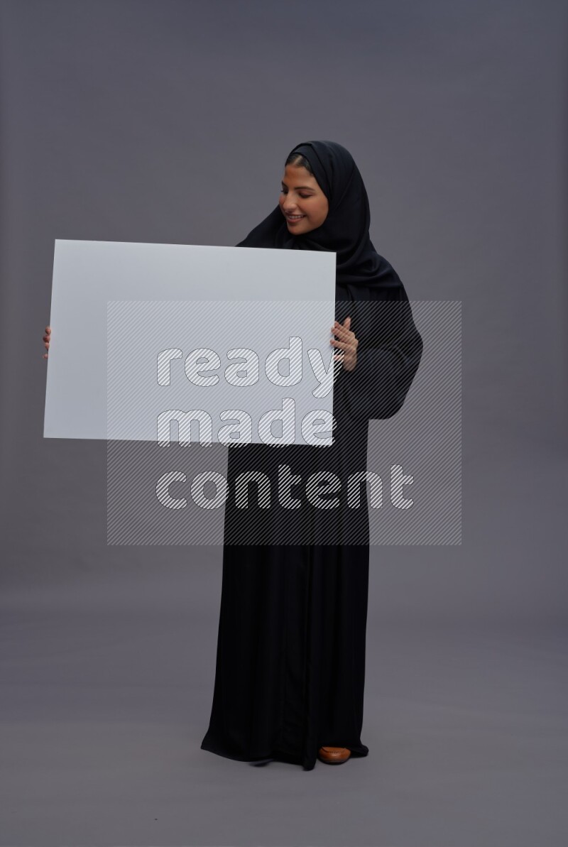 Saudi woman wearing Abaya standing holding white board on gray background