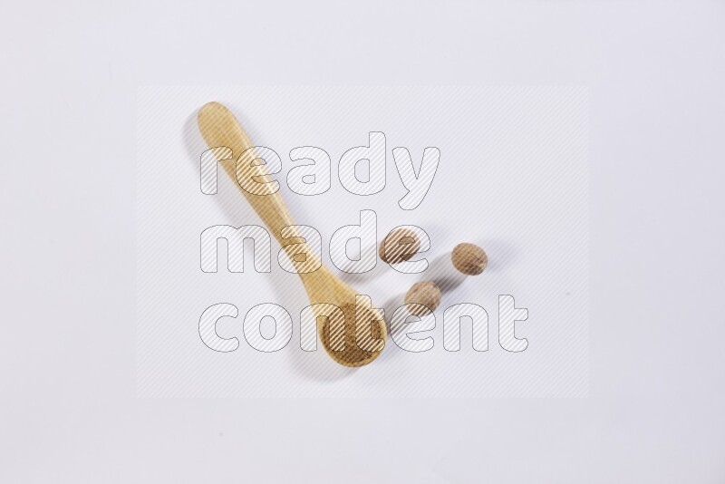 A wooden spoon full of nutmeg powder with whole nutmeg seeds beside it on a white flooring
