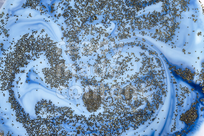 A close-up of sparkling gold glitter scattered on swirling blue background