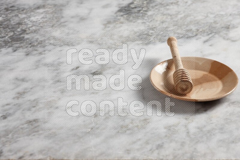 Multicolored pottery plate with wooden honey dipper in it on grey marble background