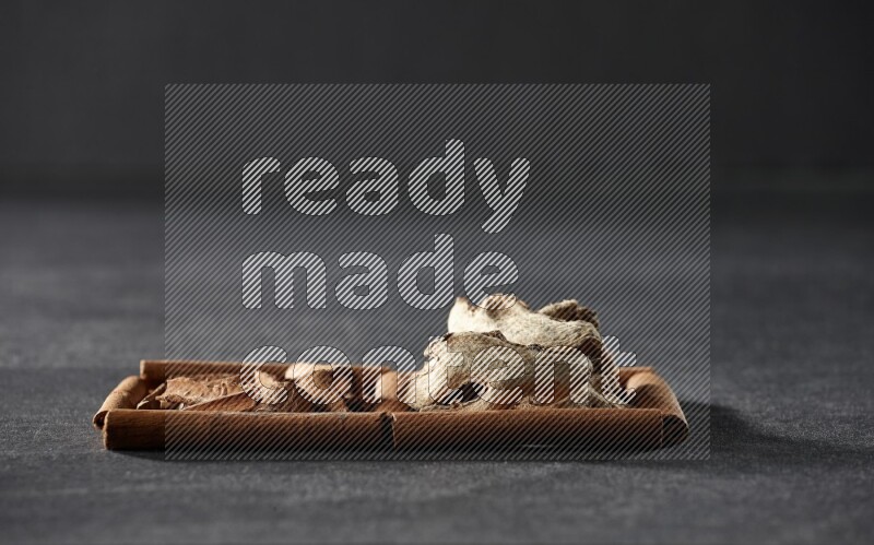 مربعان من أعواد القرفة ممتلئان بقطع من القرفة والزنجبيل المجفف علي خلفية سوداء