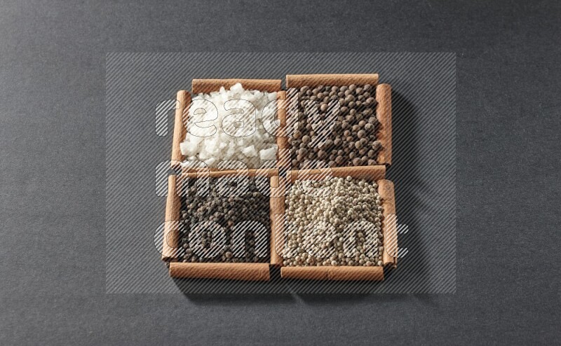 4 مربعات من عيدان القرفة ممتلئة بحبوب الفلفل الأسود والفلفل الأبيض وبهار الفلفل الحلو والملح الأبيض على أرضية سوداء
