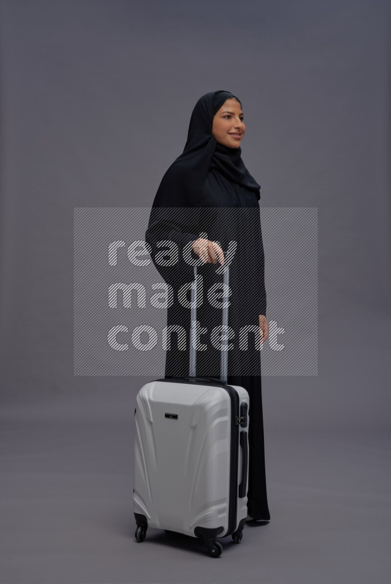 Saudi woman wearing Abaya standing holding bag on gray background