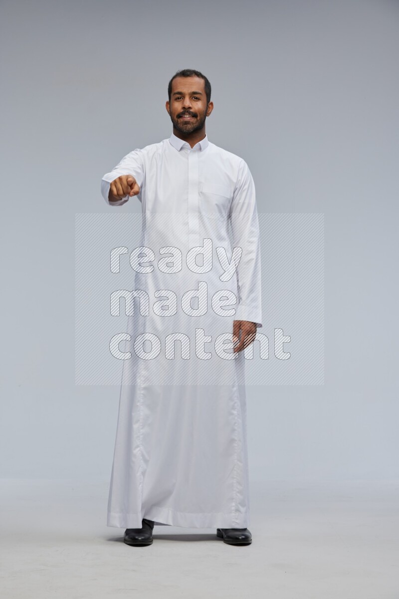 Saudi man Wearing Thob standing interacting with the camera on Gray background