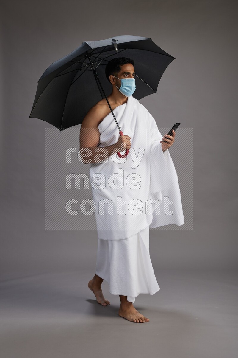 A man wearing Ehram and mask Standing holding umbrella on gray background on gray background