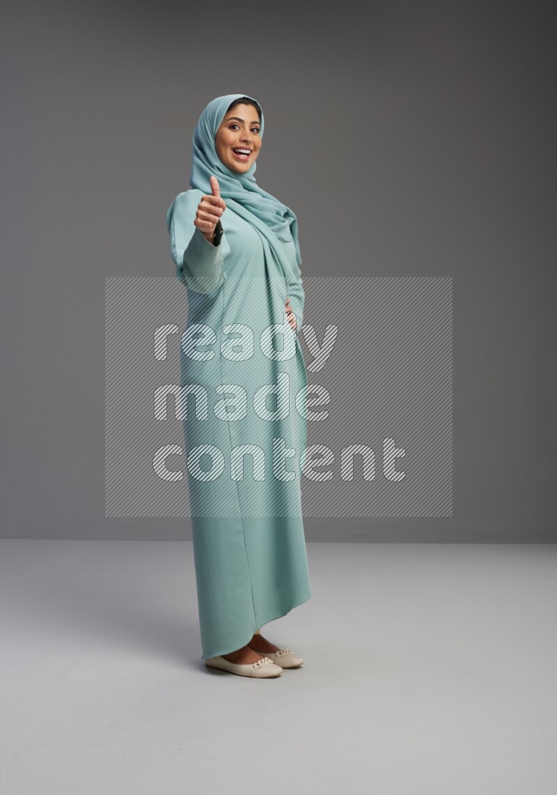 Saudi Woman wearing Abaya standing interacting with the camera on Gray background