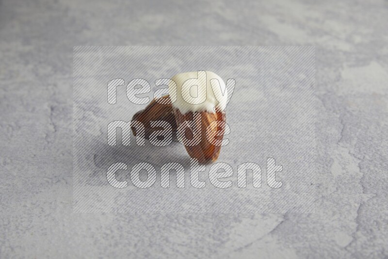 two almonds stuffed dates covered with white chololate on a light grey background