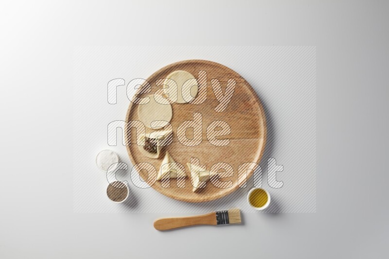 two closed sambosas and one open sambosa filled with meat while salt, black pepper and oil with oil brush aside in a wooden dish on a white background