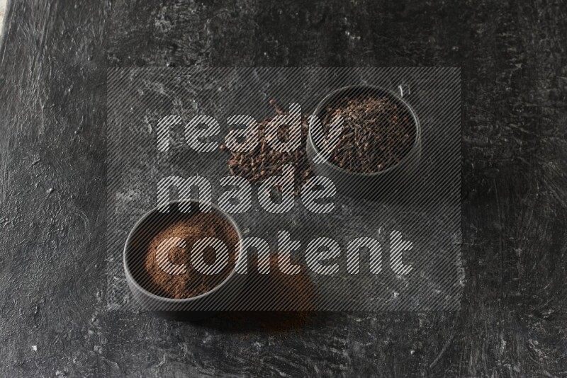 وعاءين من الفخار الأسود أحدهما ممتلئي بحبوب القرنفل والآخر ممتلئ ببودرة القرنفل على خلفية سوداء