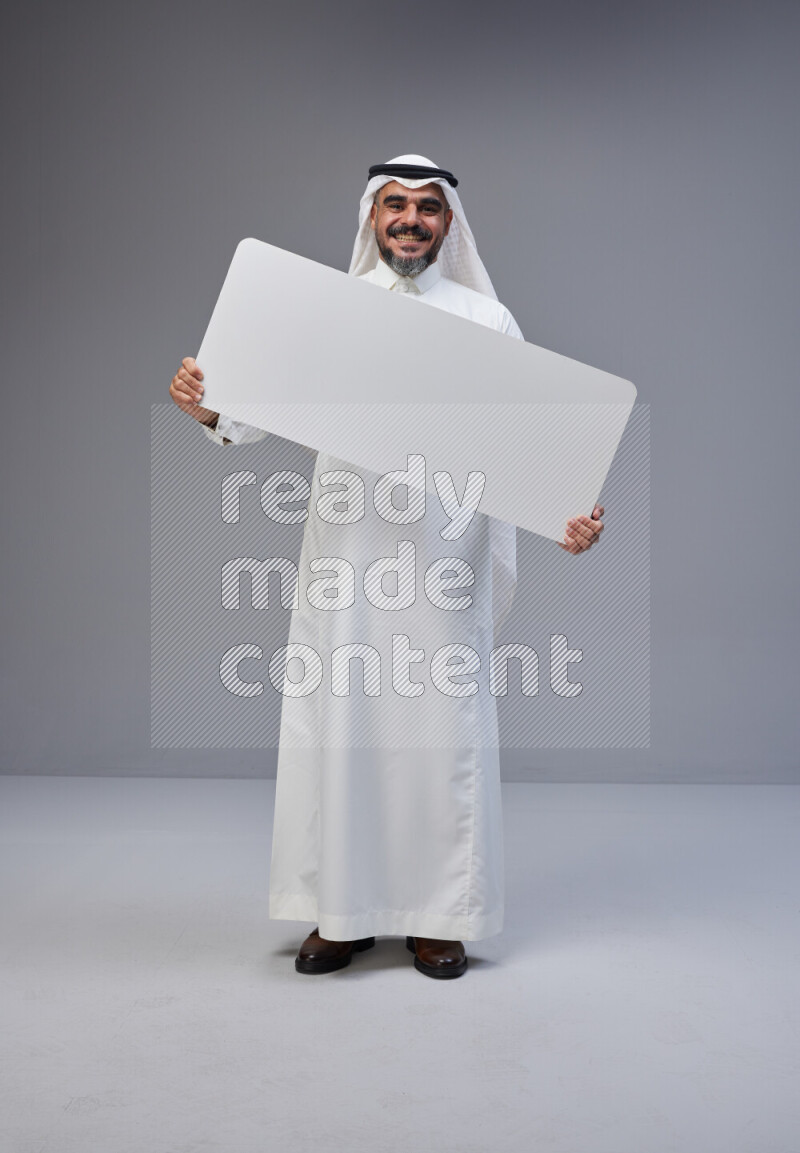 Saudi man Wearing Thob and white Shomag standing holding board on Gray background