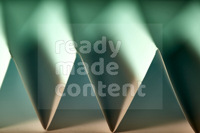 A close-up abstract image showing sharp geometric paper folds in green gradients and warm tones
