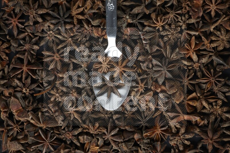 Star Anise in a metal spoon on more stars anise filling the frame on black flooring