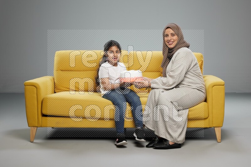 A girl sitting giving a cake to her mother on gray background