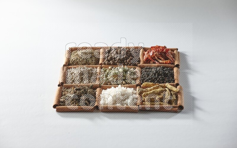 9 مربعات من أعواد القرفة ممتلئة بالهيل في المنتصف محاطة بأصابع الكركم والملح والريحان المجفف والفلفل الأبيض والكمون وبهار الفلفل الحلو والفلفل الحار المجفف والفلفل الأسود على أرضية بيضاء