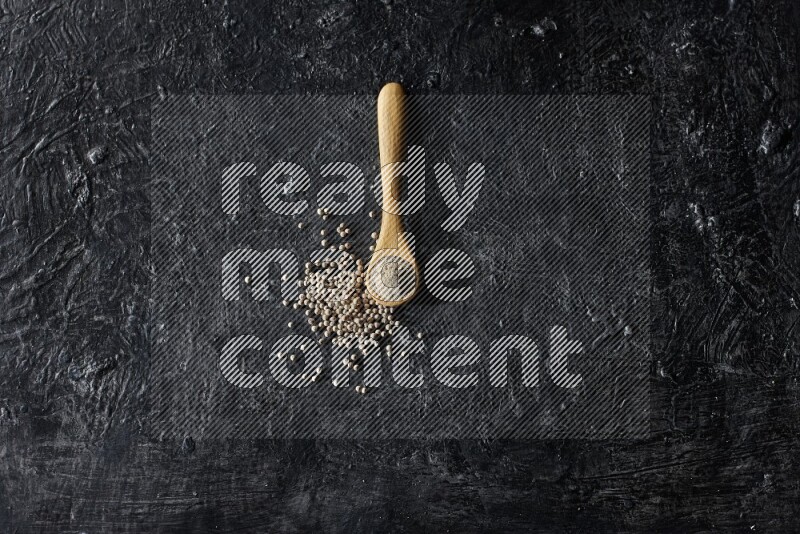 ملعقة خشبية ممتلئة ببودرة الفلفل الأبيض مع حبوب الفلفل الأبيض على أرضية سوداء