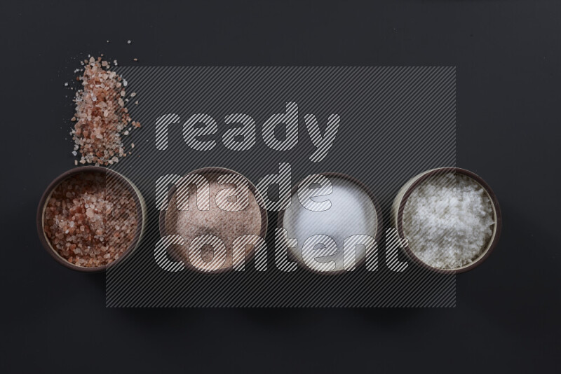 4 pottery bowls filled with himalayan salt and white salt on black background