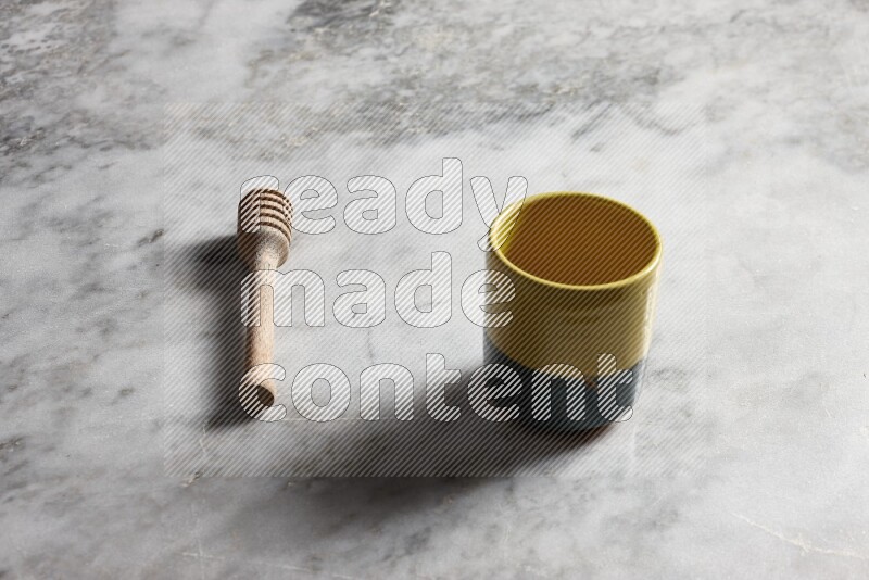 Multicolored pottery cup with wooden honey dipper on the side on grey marble background