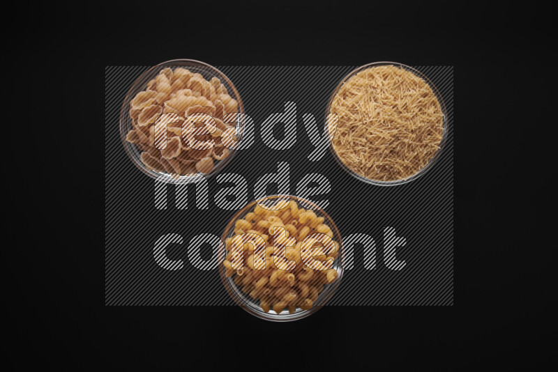 Different pasta types in glass bowls on black background