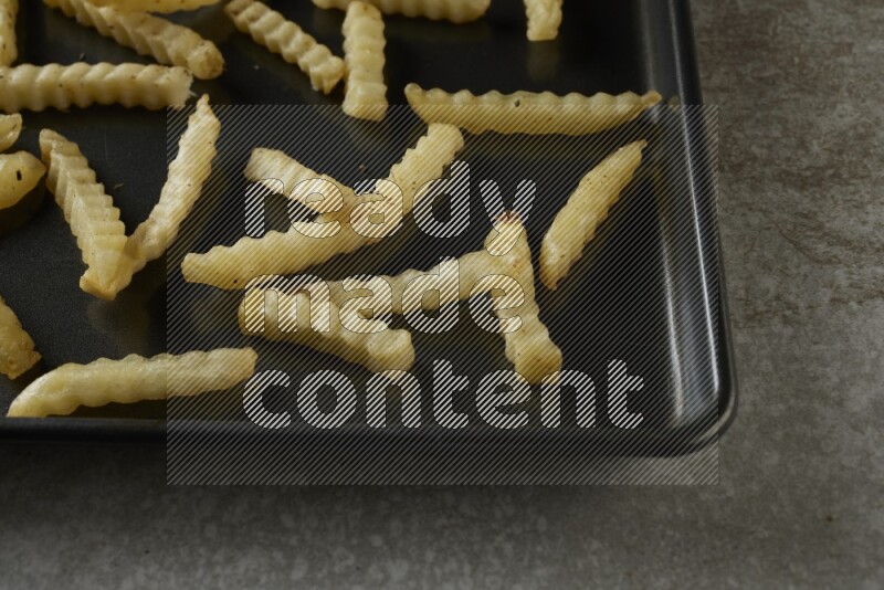 crinkle fries in a black stainless steel rectangle tray on grey textured counter top
