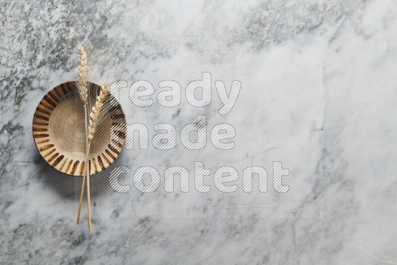 Wheat stalks on multicolored pottery plate on grey marble background