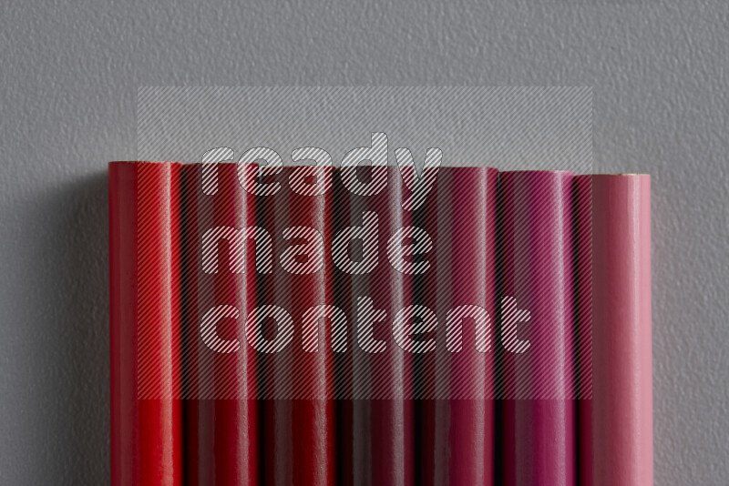 A collection of colored pencils arranged showcasing a gradient of pink and red hues on grey background