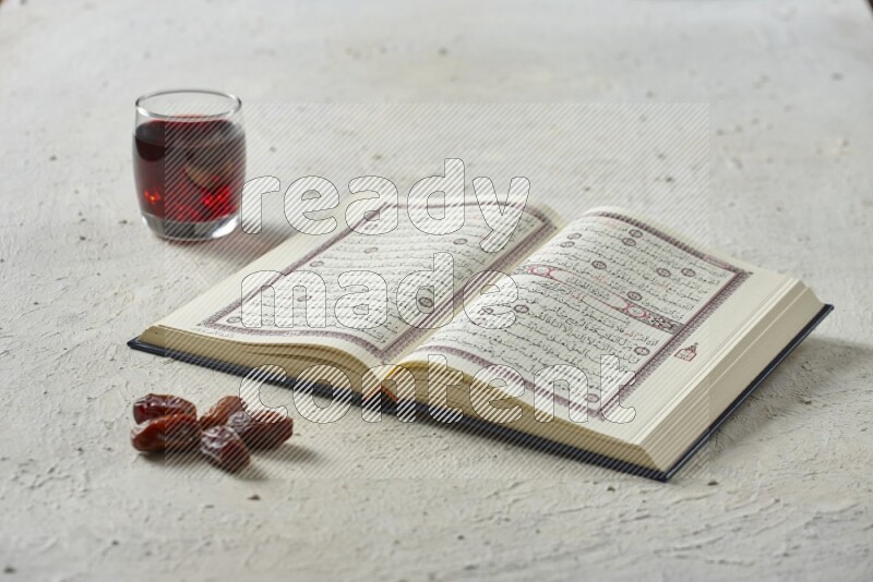 Quran with dates, prayer beads and different drinks all placed on textured white background