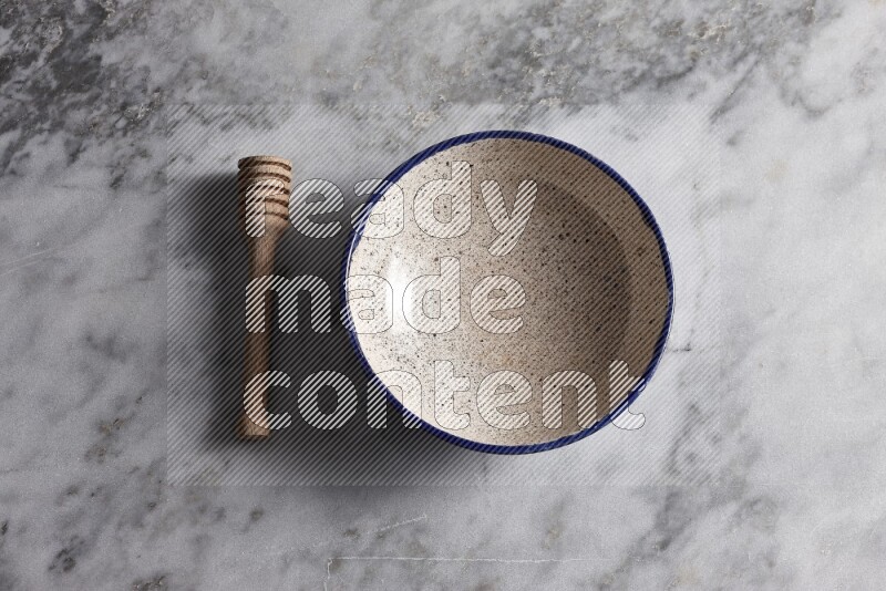 Multicolored pottery bowl with wooden honey dipper on the side on grey marble background