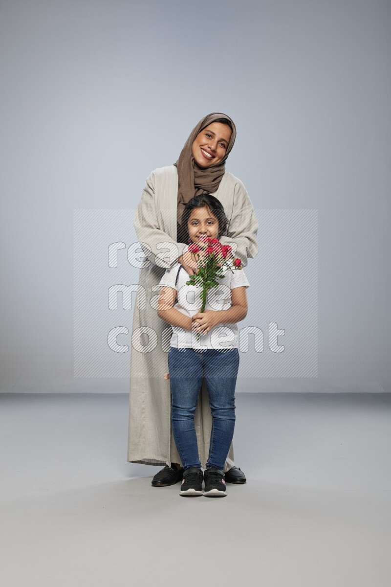 A girl standing giving flowers to her mother on gray background