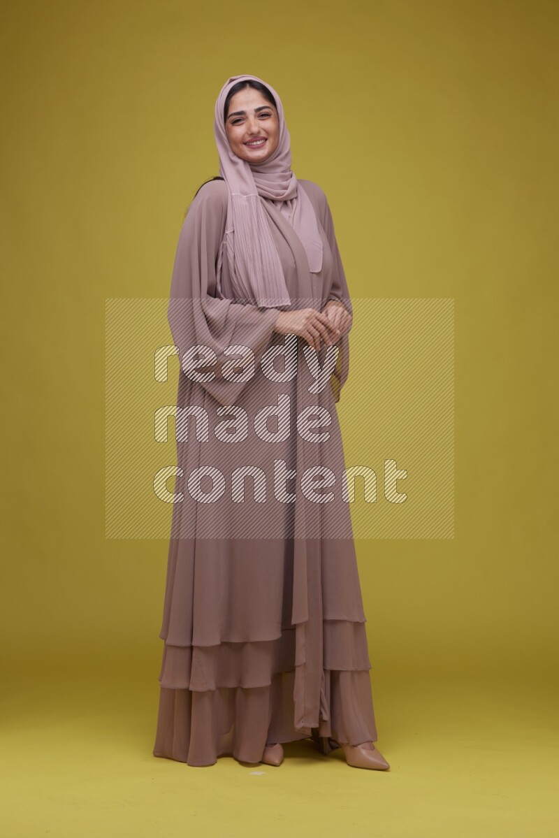 A woman Posing on a Yellow Background wearing Brown Abaya with Hijab
