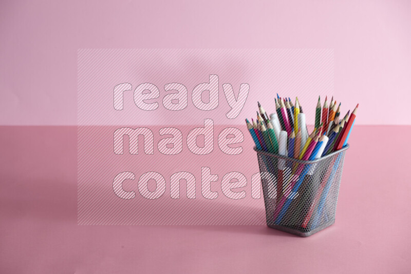 Pens, pencils and other different school supplies in a metal pen holder on rose background
