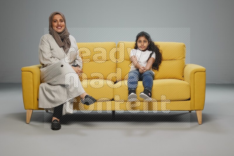 A girl with her mother sitting and interacting with the camera on gray background