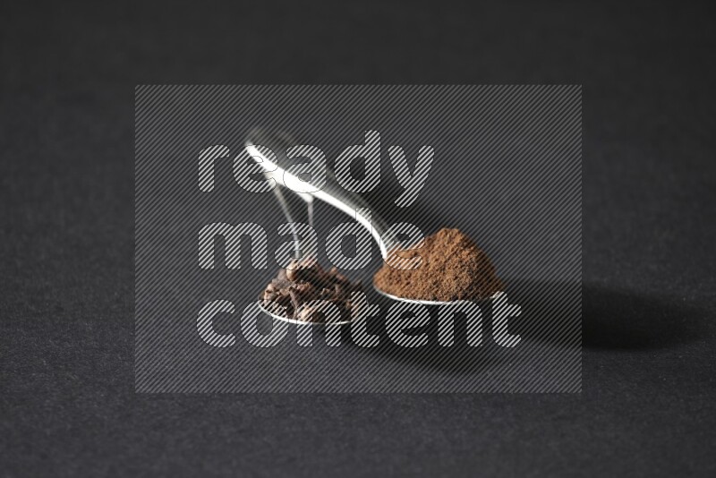 ملعقتان معدنيتان، إحداهما ممتلئة بحبوب القرنفل والأخرى ببودرة القرنفل، على خلفية سوداء