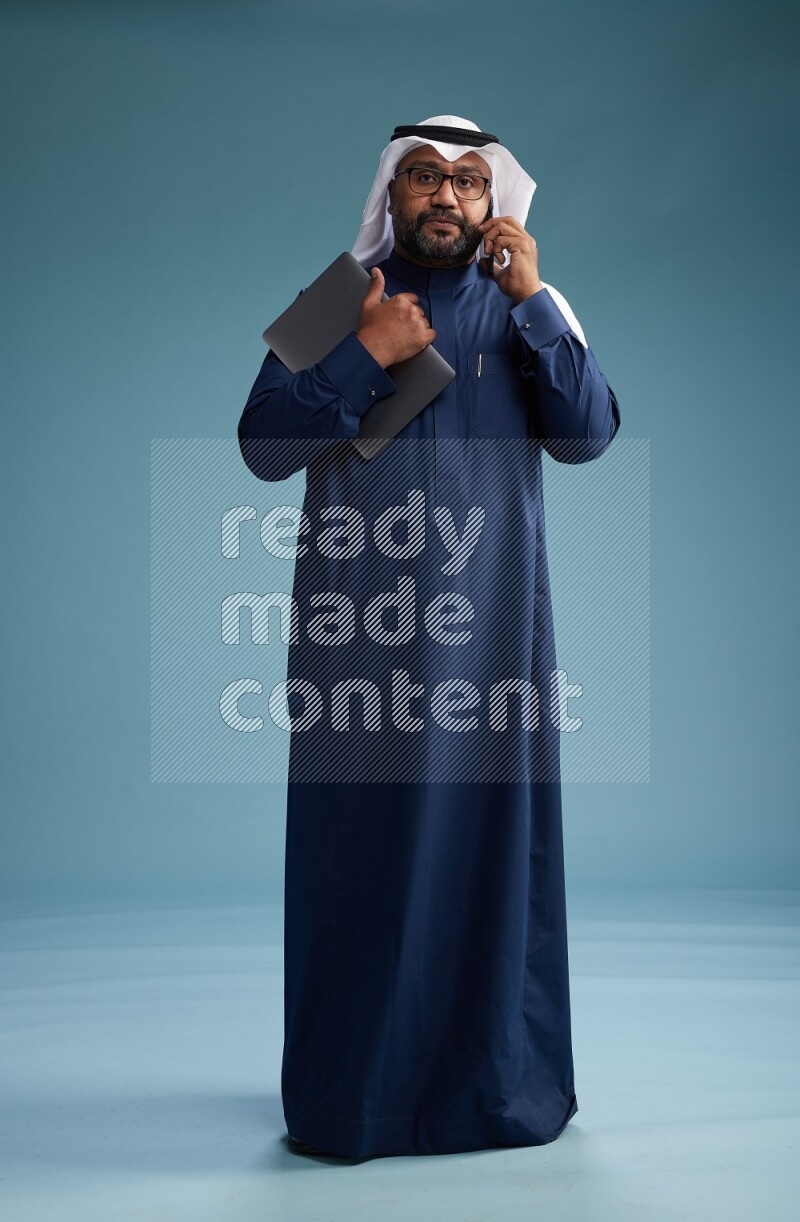 Saudi Man with shimag Standing talking on phone on blue background