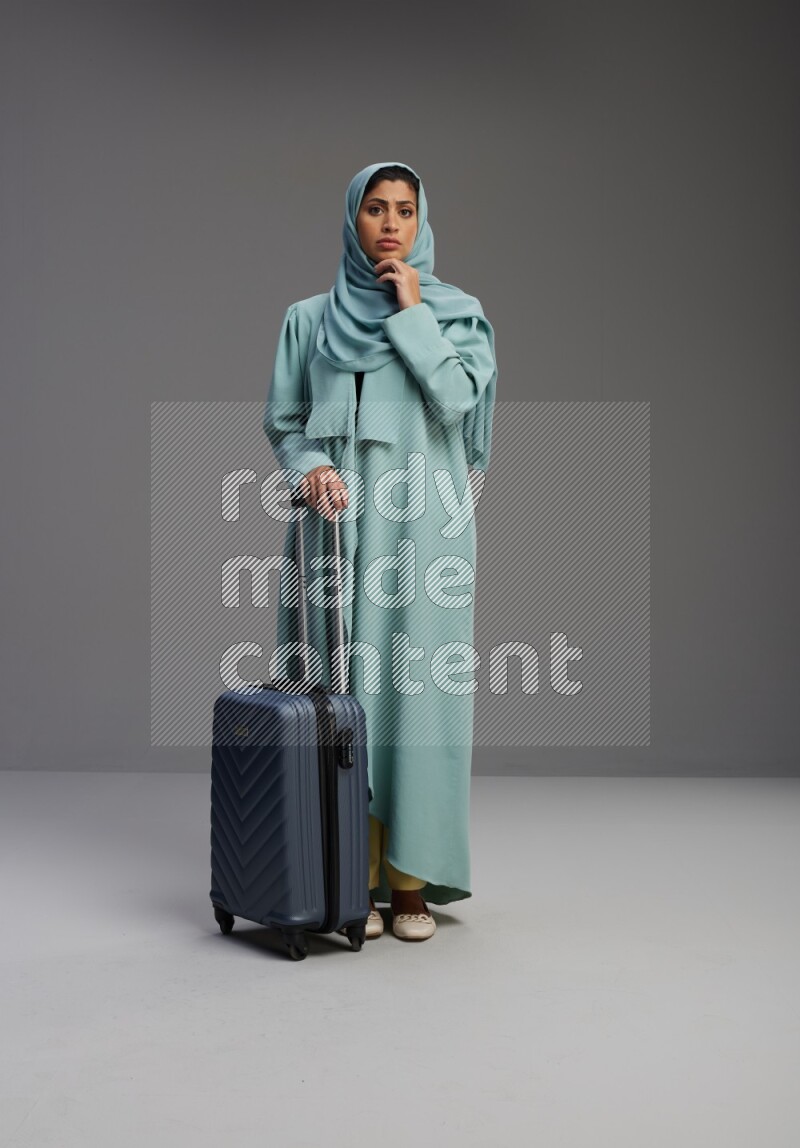 Saudi Woman wearing Abaya standing holding Travel bag on Gray background