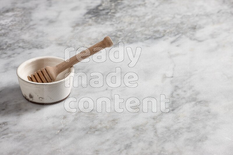 White pottery bowl with wooden honey dipper in it on grey marble background