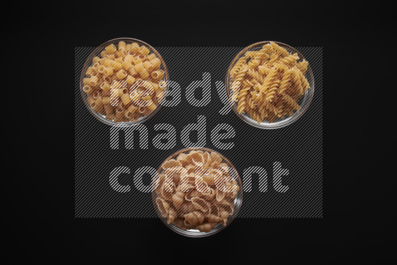 Different pasta types in glass bowls on black background