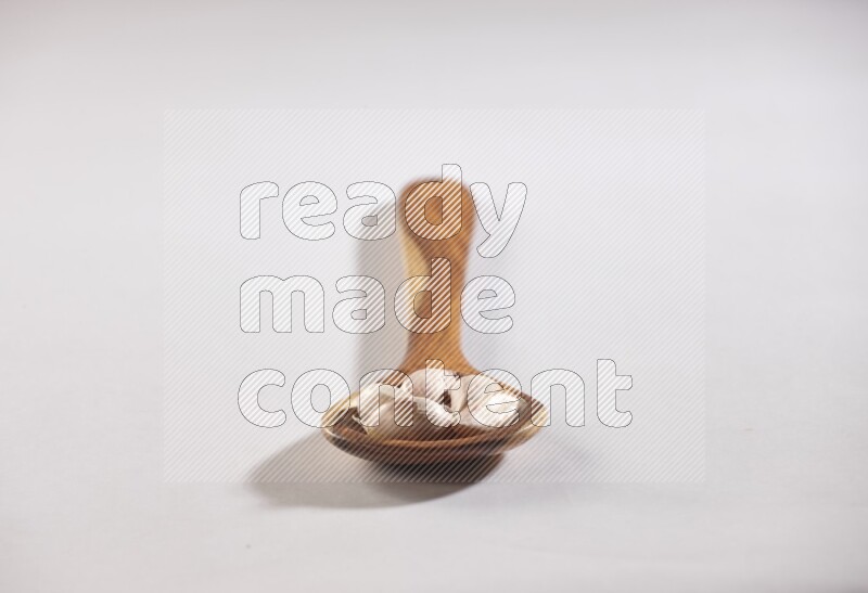 A wooden ladle full of garlic cloves with sprinkled powder on a white flooring