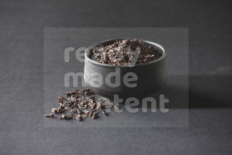 A black pottery bowl full of cloves on a black flooring
