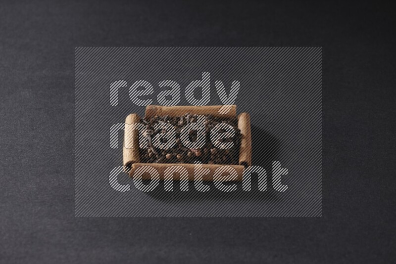 أربعة من أعواد القرفة مكونة شكل مربع بداخلها حبوب قرنفل علي خلفية سوداء
