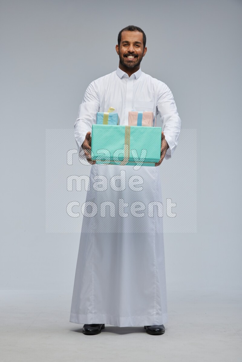 Saudi man Wearing thob standing holding gift box on Gray background